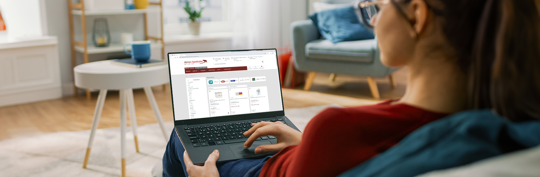 Frau sitzt auf Sofa und hält einen Laptop mit dem Shop der Bären Apotheke Grafing